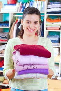 A woman smiles at the camera while holding a pile of clothing for donation