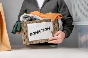 A man holding a box of clothing with the word "donation" on the front of the box