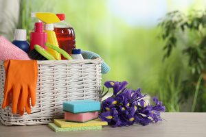 Spring cleaning supplies in a white wicker basket with a bouquet of dark purple calla lilies